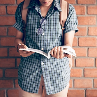 Jeune devant un mur de briques lisant un livre